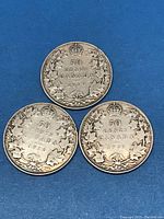 Three Canadian silver 50 cent coins dated 1916, 1918, and 1919 placed on blue background, showing reverse sides with maple leaf wreath and crown design.