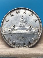 Reverse side of the 1951 Canadian silver dollar coin showing a canoe with two men and the inscriptions.