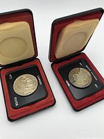 Two Canadian silver dollar coins in black and red clamshell presentation cases with cream-colored padding, showing obverse sides.