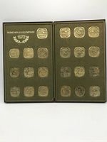 Full view of the opened green metal box displaying all 24 square shaped medallions representing different Olympic sports from 1972 Munich Olympics.