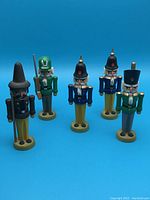 Front view of five small wooden soldier figurines standing in a group on a blue background.