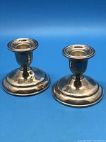 Pair of sterling silver candle holders on blue background, showing front and side views.