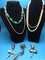 Photo showing all four necklaces and three floral brooches, displayed on black jewelry stands with blue background.