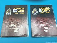 Two closed coin books titled Canada 10 Cents 1870-1929 and Canada 1 Cent 1922-1963 on blue surface.
