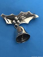 Front view of the sterling silver Christmas brooch with holly leaf and dangling bell detail, showing the design and silver finish.