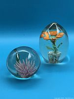 Lot showing two glass paperweights: one sphere with pink flower inside, one oval with orange flower inside