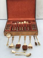 Complete 24k gold plated flatware set displayed in a wooden box with rust-colored felt lining showing most flatware organized in slots and serving pieces laid in front.
