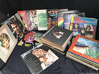 Wide view of approximately 57 vinyl record albums arranged and fanned out on a black surface, showing various album cover designs and titles including ABBA Greatest Hits and Double Clutch Adults Only.