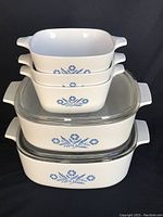 Stacked view of all five CorningWare dishes showing blue cornflower pattern and clear glass lids on two casseroles.