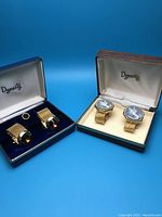 Photo of two sets of cuff links in their original Dynasty boxes against a blue background.