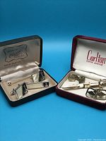 Overview photo of two men's jewelry sets including tie clips and cuff links displayed in their original boxes.