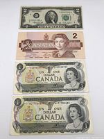 Photo of four paper banknotes including one USA $2 bill and three Canadian bills (two $1 from 1973, one $2 from 1986)