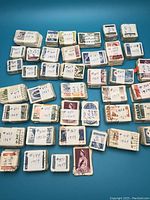 Photo showing multiple bundles of used Canadian stamps wrapped in paper bands with hand-written catalog numbers and dates of issue, stacked neatly on a flat surface.