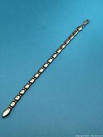 Full length view of the sterling silver bracelet placed on a blue background showing its linked chain design and lobster clasp.