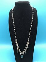 Full view of the sterling silver necklace on black display stand showing the silver chain and the two layered arrangements of blue crystal dangles.