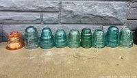 Front row view of 9 insulators showing porcelain amber and multiple green glass insulators.