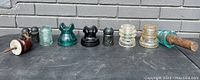 Nine antique insulators arranged in a row showing various colors, shapes, and materials including porcelain and glass.