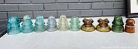 Full row of 11 insulators arranged in a line, showing varying colors and shapes from aqua blue glass to amber and green porcelain.