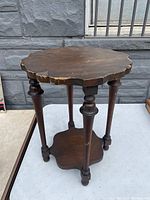 Side view of antique solid oak side table showing scalloped edge top, turned legs and lower shelf with matching shape.