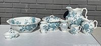 Photo showing full front view of the antique wash basin set including pitcher, large basin, covered dish and smaller items featuring blue floral pattern.