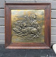 Full view of the brass dog wall plaque with walnut frame hanging against a brick wall.