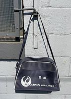Front view of navy blue Japan Airlines carry on shoulder bag with white logo and piping