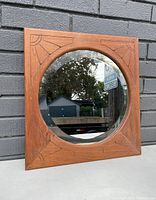 Front view of square oak frame with circular inset mirror and carved geometric patterns in wood corners.