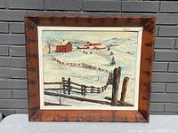 Framed oil on board painting showing a winter scene with red barn, fences, and snow-covered hills.