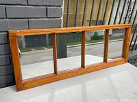 Horizontal wall hanging mirror with antique pine wood frame showing four vertical glass panels, placed outdoors against a brick wall.