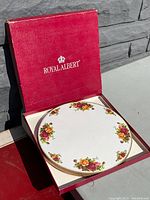 Royal Albert Old Country Roses heat resistant casserole stand trivet in original red box outdoors on wooden surface.