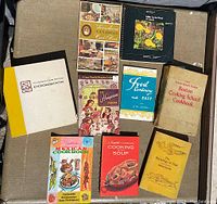 Photo of all nine vintage cookbooks arranged on a surface, showing varied conditions and colorful covers.