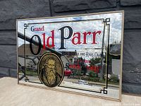 Front view of vintage Grand Old Parr Deluxe Scotch Whisky advertising mirror with gold framed ornate border, oval portrait and detailed text.