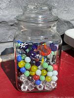 Vintage clear glass jar with lid filled with colorful marbles and spherical glass balls photographed outdoors with bright lighting