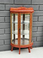 Front and angled view of vintage red and gold painted faux Louis XV tabletop showcase cabinet with curved glass panels and mirrored backing.