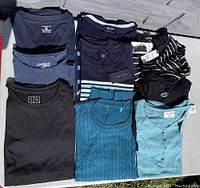 Top-down view of folded women's shirts and sweaters, showing variety including black, blue, striped, and teal garments.