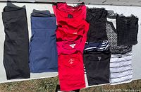 All clothing items laid out flat on a surface, including leggings and various tops in red, black, white, blue colors and patterns.