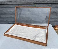 Opened view of the vintage wooden showcase with hinged plexiglass door revealing the padded white fabric interior base.