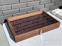 Wooden showcase with visible wear, glass top, and metal lock on front, photographed at an angle showing depth and wear.