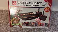 Box front of Atari Flashback 5 classic game console showing console image, 2 joystick controllers, and game titles.