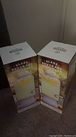 Two boxed glass beverage dispensers about 2 feet tall each.