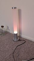 Tall cylindrical LED floor lamp powered and lit, showing warm light color.