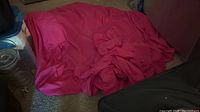 Photo of a bright pink fabric piece on the floor, likely a tablecloth or large napkin.