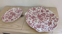 Two oval plates with red English Chippendale floral pattern placed side by side on a wooden surface