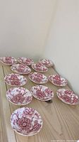 Set of 12 small English Chippendale bowls arranged on a wooden surface, showing floral red pattern on white.