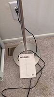 Bottom section of the lamp showing base, lower metal pole, power cord, and FLUGBO instruction manual.