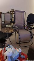 Set view showing reclining taupe mesh chair, round glass top side table, and part of foot stool