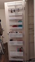 Full view of the storage racks mounted on a white door, showing multiple adjustable clear storage bins with various items inside including keys and small household items.