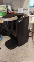 Side view of black Keurig K-Cup coffee maker on kitchen counter, showing removable drip tray and water reservoir.