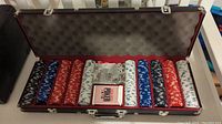 Open carrying case showing five stacks of poker chips in various colors, a dealer button, and a full deck of cards.