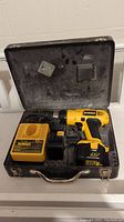 Open metal carrying case showing yellow and black DeWalt cordless drill, charger, and battery inside